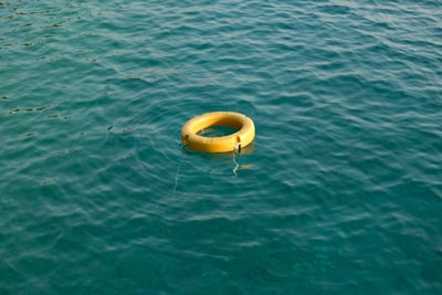 image: A bright yellow lifebuoy floating calmly on the crystal-clear turquoise sea. Captured during a serene summer day, this minimalist image emphasizes safety and tranquility amidst open water. Ideal for themes around marine safety, summer, or solitude.